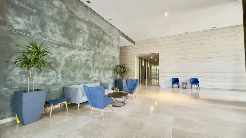 Room features: grey textured wall, light beige stone wall, marble flooring, two blue upholstered chairs, grey fabric sofa, round coffee table, potted plant in large planter, potted plant in small planter, large windows allowing natural light, recessed ceiling lights; style: modern.
