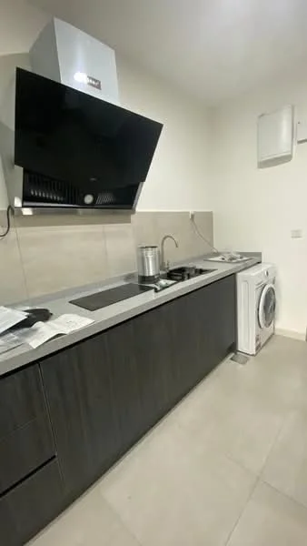 Kitchen features: grey granite countertop, black wall-mounted range hood, stainless-steel sink, 4-burner gas hob, built-in oven, white front-load washing machine, dark wood cabinetry, light grey tile flooring, wall-mounted air conditioning unit, neutral painted walls; style: modern.