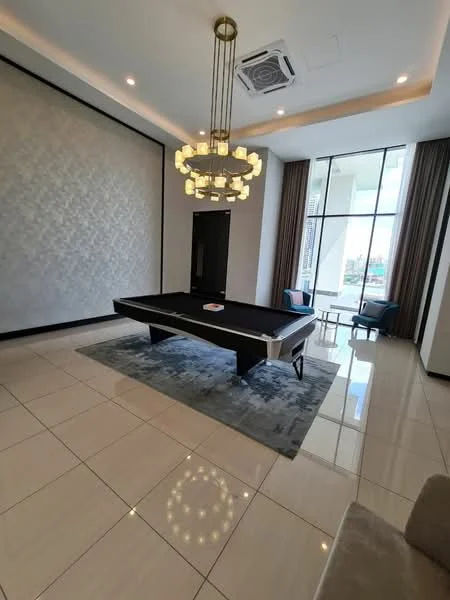 Room features: large rectangular pool table, chandelier with multiple bulbs, white painted walls, cream tiled flooring, floor-to-ceiling windows, curtains in beige, two accent chairs in blue, decorative area rug with geometric pattern, wall-mounted air conditioning unit, recessed lighting; style: modern; view: city.