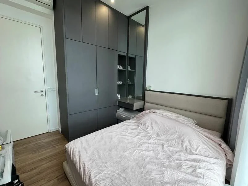 Bedroom features: queen-size bed with light pink bedding, built-in wardrobe with grey finish, nightstand with drawer, laminate flooring, white walls, window with sheer curtains, recessed ceiling lights, mirror on wardrobe, air conditioning unit; style: modern.