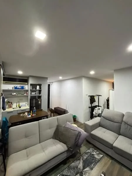 Living features: light grey fabric 3-seater sofa, coffee table, dining table with 4 chairs, open shelving unit, refrigerator, kitchen area with countertop, recessed LED downlights, wooden flooring, white painted walls, laundry rack, decorative area rug; style: modern.