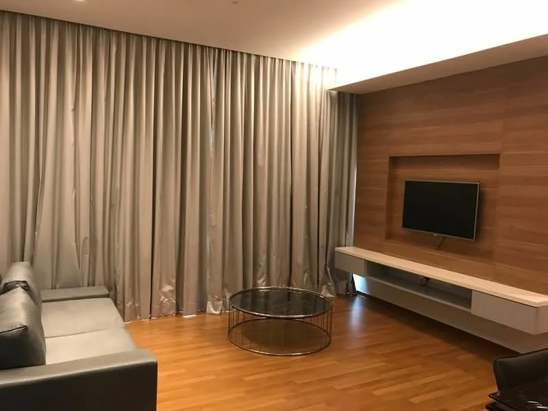 Living features: grey leather sofa, round glass coffee table, wooden TV console, wall-mounted TV, light wood accent wall, floor-to-ceiling curtains in grey, laminate flooring, recessed ceiling lights; style: modern.