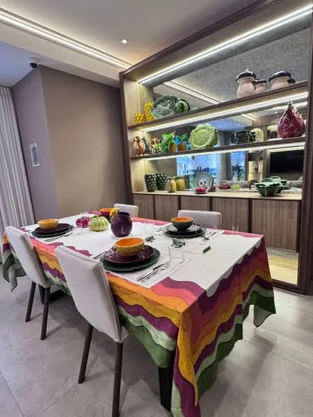 Dining features: 6-seater dining table, tablecloth with colorful stripes, ceramic dinnerware in various colors, glassware, decorative bowls, wooden cabinetry, open shelving with decorative items, large window with natural light, neutral wall color, tile flooring; style: modern; view: garden.