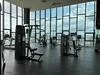 Room features: large floor-to-ceiling windows, city skyline view, modern gym equipment, weight machines, cardio machines, rubber flooring, high ceilings, natural light, open layout, mirrored wall; style: modern; view: city.