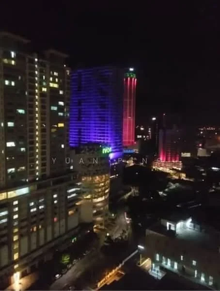 Exterior type: high-rise condominium; features: illuminated facade, glass curtain wall, multiple storeys, surrounded by urban landscape, night view, city skyline in background; style: modern.