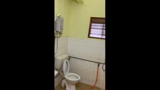 Bathroom features: white tiled walls, light yellow painted walls, ceramic tile flooring, one-piece toilet, shower with water heater, window with horizontal slats, grab bar, toilet paper holder.