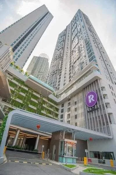 Exterior type: high-rise condominium; features: glass curtain wall, exposed concrete facade, recessed balconies, feature lighting at night, double-volume main lobby, manicured landscaping, driveway with interlocking pavers, guard house at entrance; style: modern.