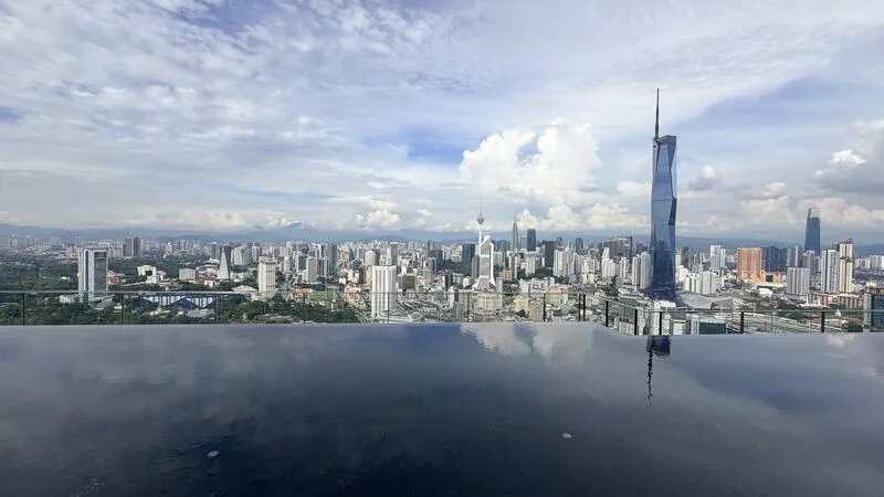 Exterior type: high-rise condominium; features: infinity pool, city skyline view, surrounded by urban landscape, glass railing, rooftop terrace, cloudy sky, modern architecture; style: modern.