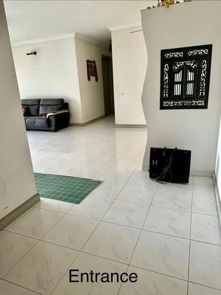Room features: white walls, marble tile flooring, sofa in grey, decorative wall panel, green mat at entrance, light fixture on wall, doorway leading to another room.