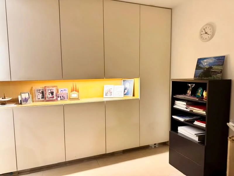 Room features: built-in cabinetry with lighted display, cream cabinetry, dark wood shelving unit, wall clock, decorative items on shelves, photographs in frames, neutral wall color, tile flooring; style: modern.