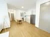 Room features: light wood flooring, white painted walls, recessed downlights, kitchen cabinetry, stainless-steel fridge, kitchen countertop, dining table, open layout, doorway leading to another room; style: modern.