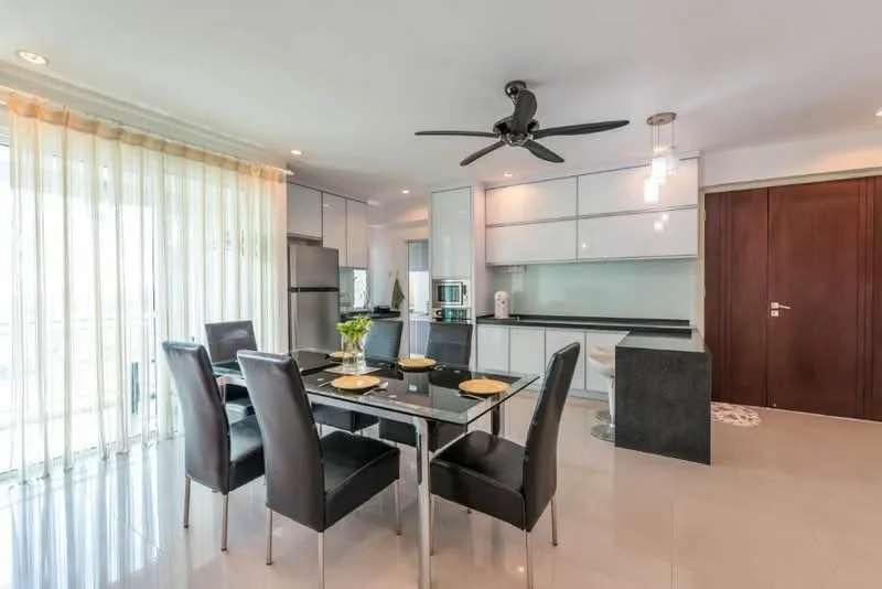 Dining features: glass dining table, 6 black upholstered dining chairs, pendant light fixture, 5-blade ceiling fan with light, white cabinetry, black countertop, stainless-steel fridge, built-in oven, microwave, sliding glass door, sheer curtains, tile flooring, recessed downlights; style: modern; view: city. Kitchen features: black countertop, white cabinetry, built-in oven, microwave, stainless-steel fridge, recessed downlights; style: modern.