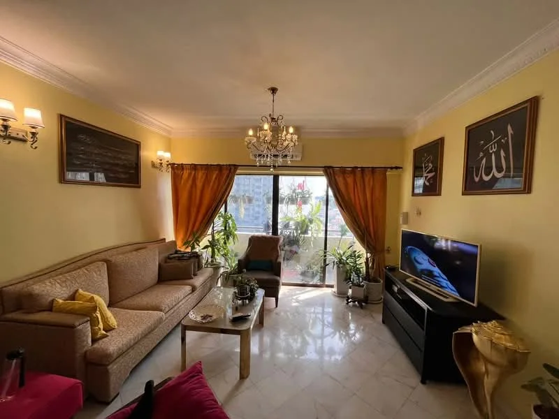 Living features: cream painted walls, marble flooring, chandelier, 2-seater fabric sofa in beige, coffee table, TV console, wall-mounted TV, floor-to-ceiling windows, sheer curtains, decorative plants, framed artwork, area rug with geometric pattern, crown moulding; style: contemporary; view: city.