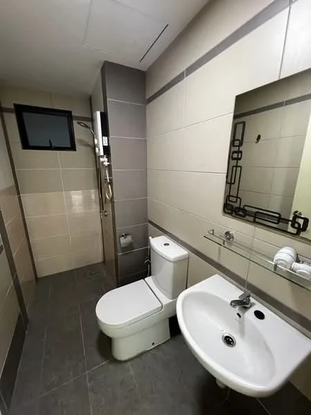 Bathroom features: grey ceramic tile flooring, light beige wall tiles, dark grey accent wall, one-piece toilet, chrome basin mixer faucet, round sink, mirror with decorative frame, shower area with handheld shower, glass shower partition, towel rack, window for natural light; style: modern.