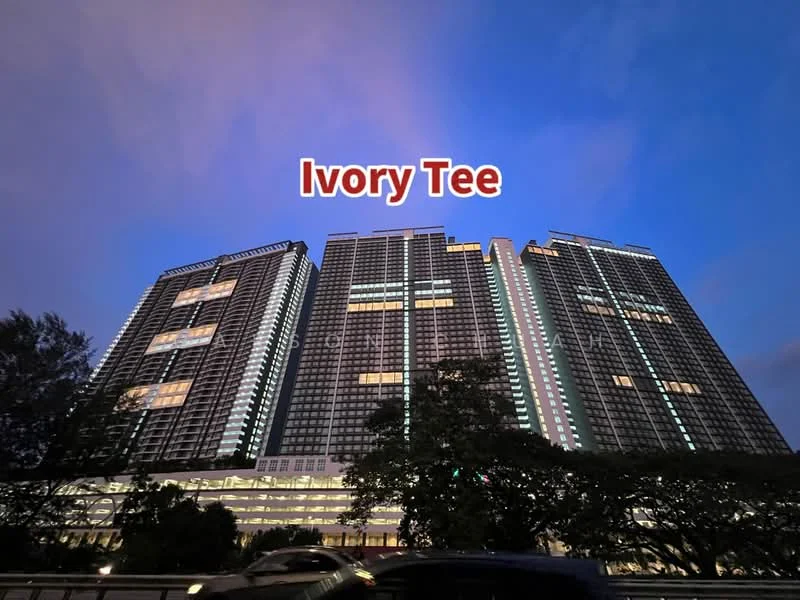 Exterior type: high-rise condominium; features: glass curtain wall, illuminated facade, multiple recessed balconies, landscaped grounds, surrounded by trees, parking deck visible, urban context with road in foreground; style: modern.