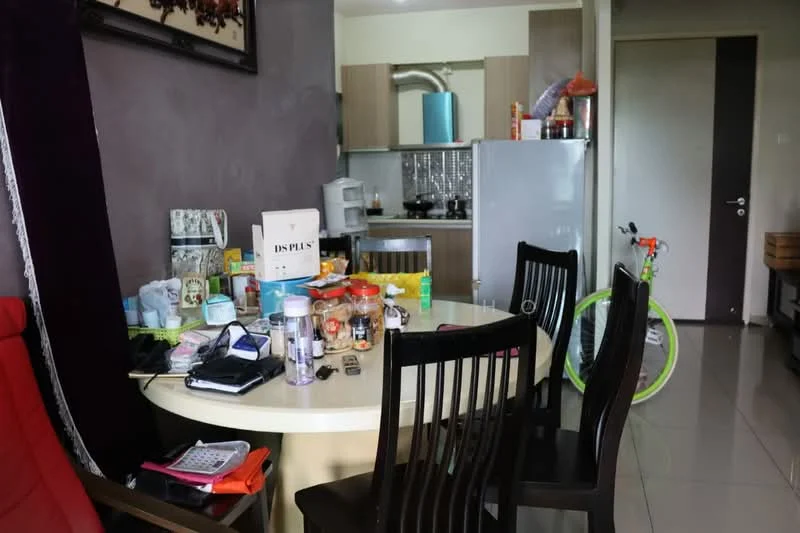 Dining features: round dining table, 4 black dining chairs, various food items on table, white ceramic plates, glass jars, bottles, kitchen appliances visible in background, green bicycle in background, grey walls, tile flooring, wooden cabinetry in background, refrigerator in background.