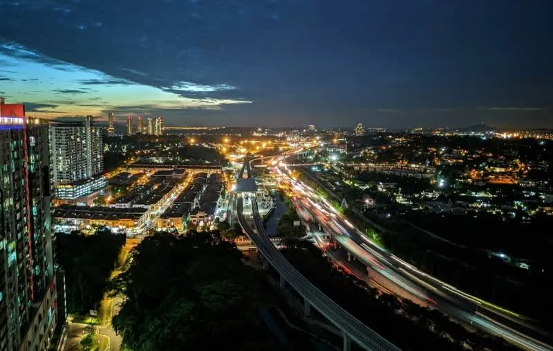 Exterior type: high-rise condominium; features: city skyline view, nighttime lighting, surrounding urban landscape, visible highways, traffic flow, mixed-use development, high-rise buildings in the background, greenery at the base; style: modern.