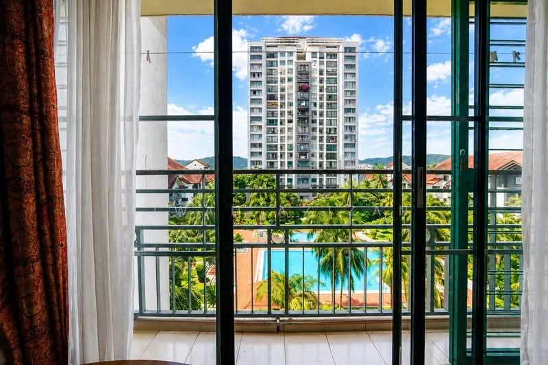 Room features: floor-to-ceiling windows, sheer curtains, balcony with railing, tile flooring, view of swimming pool, view of surrounding greenery, city skyline in background, natural light; style: modern; view: pool.