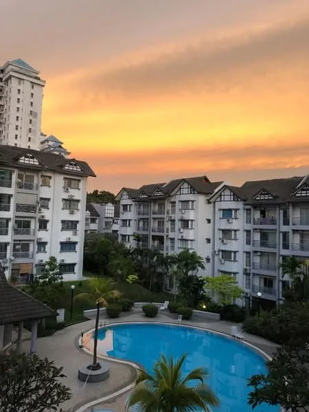 Exterior type: low-rise apartment block; features: white painted facade, recessed balconies, landscaped garden with palm trees, swimming pool with circular shape, pool deck with loungers, manicured lawn, surrounded by mature greenery, multiple storeys, gated entry, urban context with sunset view; style: modern.