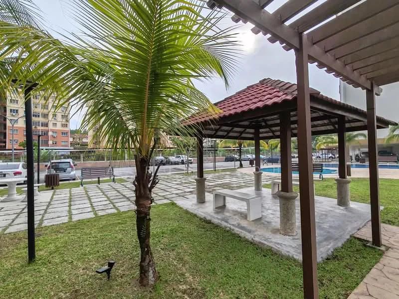 Exterior type: landscape garden; features: pavilion with tiled roof, concrete table with stone legs, manicured lawn, paved walkway, palm trees, swimming pool visible in background, surrounding greenery, parking area visible, fenced perimeter; style: tropical-modern.