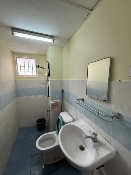 Bathroom features: white painted walls, blue tiled wall cladding, white ceramic floor tiles, single-sink vanity with chrome faucet, one-piece toilet, shower with handheld showerhead, framed mirror, wall-mounted towel rack, window for natural light, ceiling-mounted fluorescent light.