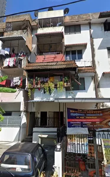 Exterior type: low-rise apartment block; features: 3-storey building, balconies with plants, exposed concrete facade, red brick accents, metal railings on balconies, multiple air conditioning units, laundry hanging on balconies, car parking area, gated entrance, ground floor commercial signage; style: traditional.