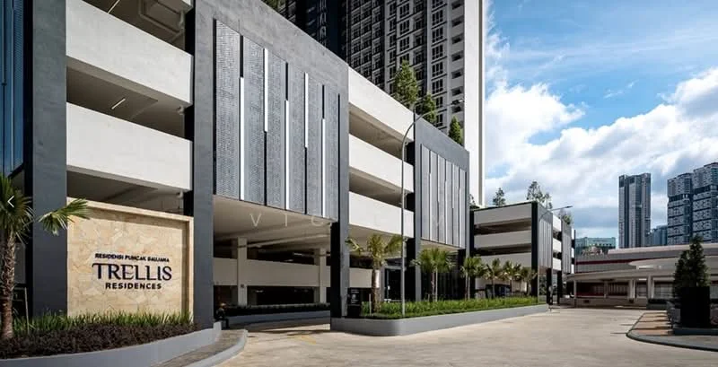 Exterior type: multi-storey car park; features: grey concrete facade, white painted facade, feature wall with decorative panels, landscaped planters with palm trees, manicured lawn, driveway with smooth surface, surrounded by high-rise buildings, signage for Trellis Residences; style: modern.