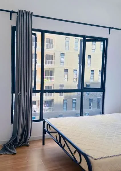Bedroom features: floor-to-ceiling windows, grey curtains, wooden flooring, metal bed frame, unmade bed with mattress, neutral wall color, visible balcony view, natural light; style: modern; view: courtyard.