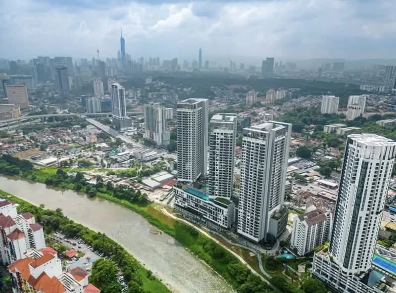 Exterior type: high-rise condominium; features: multiple high-rise buildings, riverfront view, urban skyline in background, green landscaping along riverbank, swimming pool visible on one building, balconies on buildings, surrounding residential area, city infrastructure visible, cloudy sky, modern architectural design; style: modern.
