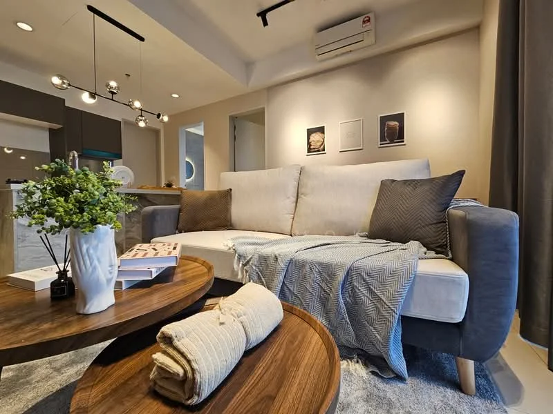 Living features: 3-seater fabric sofa in light grey, 2 accent pillows in dark grey, coffee table with wooden surface, decorative throw blanket in beige, decorative plant in white vase, wall-mounted air conditioning unit, recessed ceiling lights, grey curtains, framed artwork on the wall, open layout to kitchen area; style: modern.