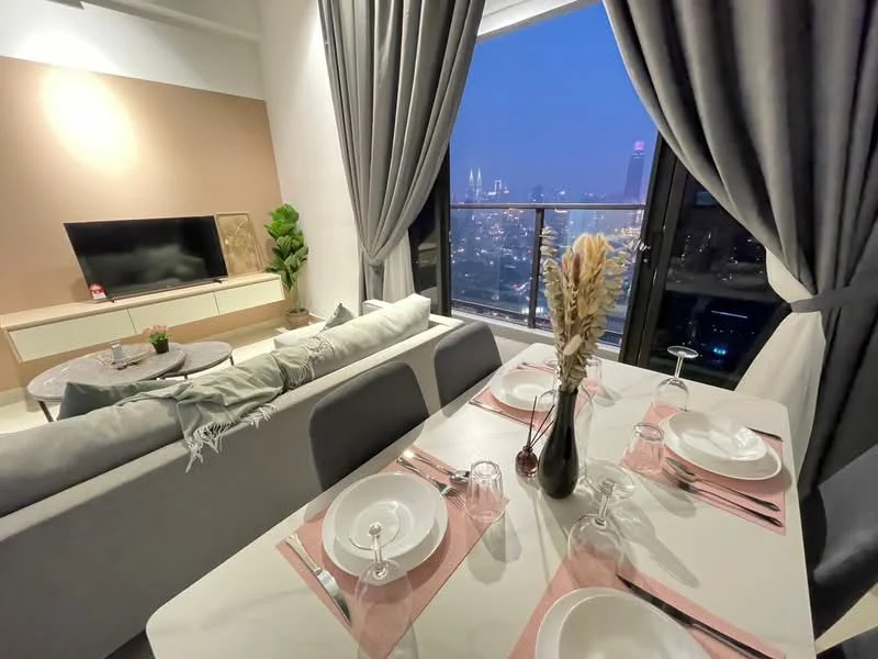 Dining features: 6-seater dining table, white table with grey placemats, glassware on the table, decorative vase with flowers, grey upholstered dining chairs, city skyline view through large windows, curtains in grey fabric, wall-mounted TV, light-colored sideboard, decorative plant in the corner, sofa in light grey fabric, throw pillows in various colors; style: modern; view: city.