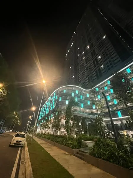Exterior type: high-rise condominium; features: glass curtain wall, illuminated facade with blue lighting, manicured landscaping, trees along the walkway, street lighting, wide pedestrian pathway, modern architectural design, multiple storeys, balconies visible, surrounded by greenery; style: modern.