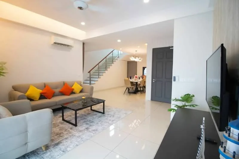 Living features: 3-seater fabric sofa in light grey, yellow and orange accent cushions, glass coffee table, area rug with geometric pattern, wall-mounted TV, ceiling fan, recessed LED downlights, white painted walls, polished tile flooring, decorative plant in ceramic pot, open layout to dining area; style: modern. Dining features: dining table with multiple chairs, chandelier lighting, open layout to living area, white walls, polished tile flooring; style: modern.