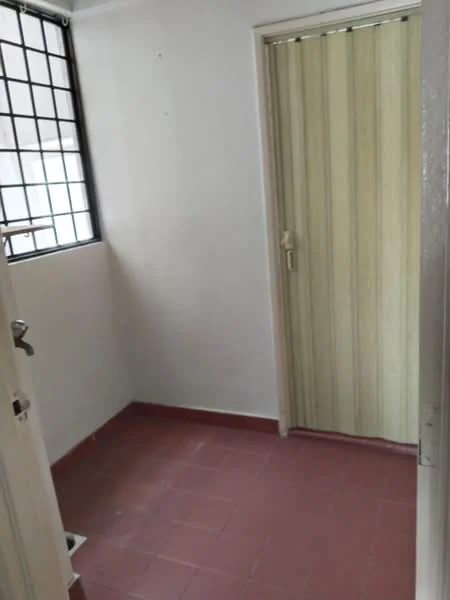 Room features: white painted walls, red ceramic tile flooring, window with grid pattern, wooden door with vertical stripes, door handle, floor drain.