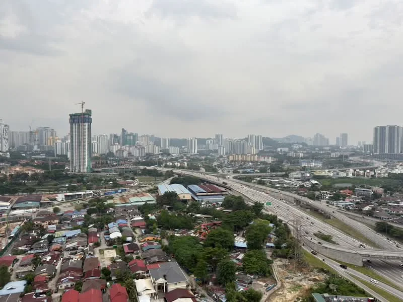 Exterior type: high-rise condominium; features: city skyline view, highway visible, mixed residential and commercial buildings, construction site in the foreground, greenery and trees in the landscape, urban setting; style: modern.