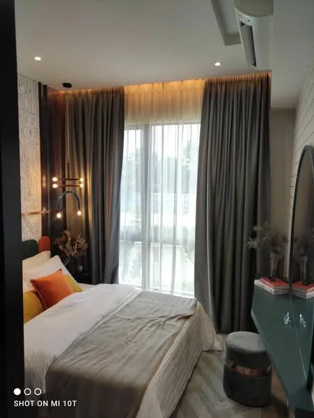 Bedroom features: queen-size bed with white bedding, upholstered headboard, two decorative pillows in orange and yellow, floor-to-ceiling windows with sheer curtains, grey curtains, wooden flooring, wall-mounted light fixture, decorative wall art, green bedside table, round ottoman, wall-mounted TV, shelf with decorative items; style: modern; view: garden.