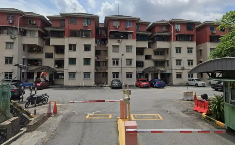 Exterior type: low-rise apartment block; features: red and cream painted facade, multiple storeys, balconies on upper floors, parking area in front, security gate at entrance, surrounded by greenery, visible air conditioning units, driveway with interlocking pavers; style: modern.