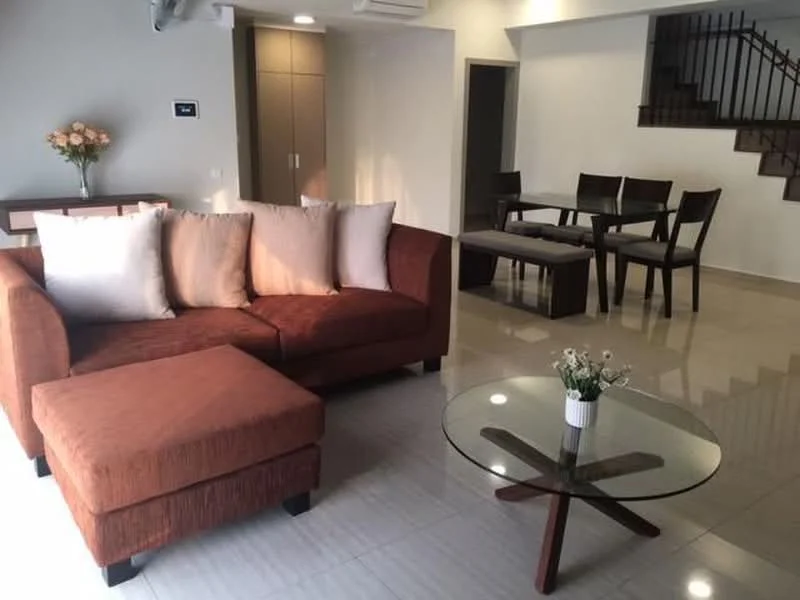 Living features: brown fabric sectional sofa, cream throw pillows, glass coffee table with wooden base, polished tile flooring, white painted walls, recessed downlights, air conditioning unit, decorative flower arrangement, dining table with four chairs, staircase in background; style: modern.