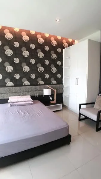 Bedroom features: queen-size bed with grey bedding, upholstered headboard, decorative wallpaper with floral pattern, white built-in wardrobe with sliding doors, nightstand with lamp, armchair in black and beige, polished tile flooring, recessed ceiling lights; style: modern.