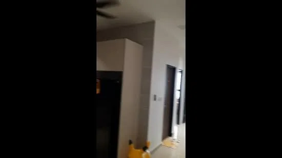 Room features: white painted walls, tile flooring, ceiling fan, black refrigerator, dark wooden door, light-colored mat, decorative item on floor.