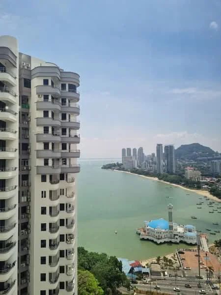 Exterior type: high-rise condominium; features: curved glass facade, white painted facade, multiple balconies, surrounded by water, city skyline in background, view of coastline, nearby high-rise buildings, greenery at base; style: modern.