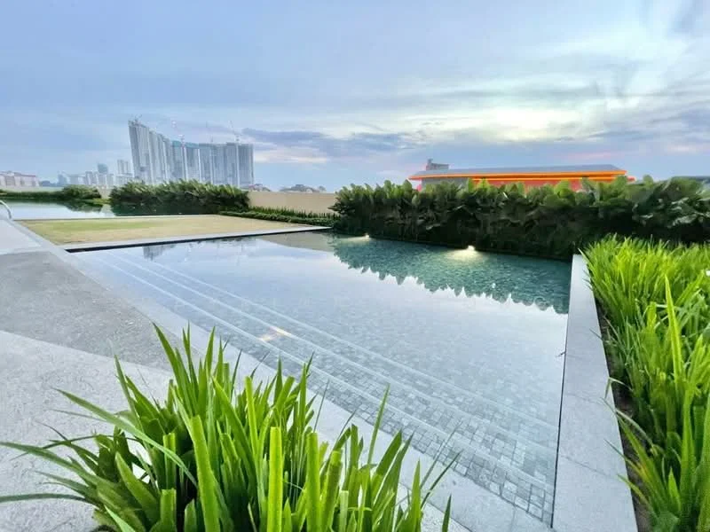 Exterior type: swimming pool deck; features: infinity edge pool, landscaped garden with greenery, paved walkway, city skyline in background, water feature, sunset lighting; style: modern.
