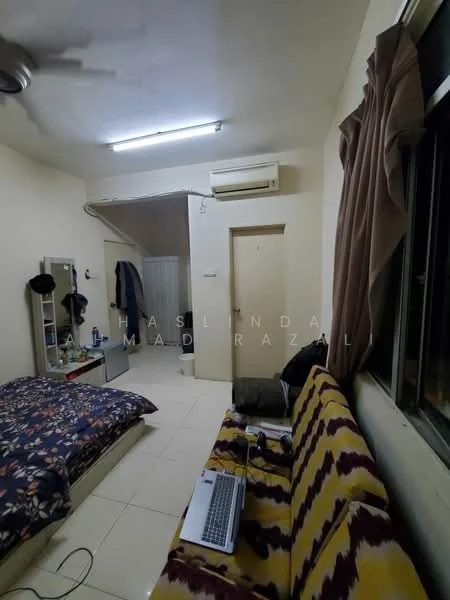 Room features: single bed with floral bedding, sofa with yellow and purple pattern, wall-mounted split AC, ceiling fan, white painted walls, tile flooring, window with brown curtains, mirror on dresser, desk with laptop, door leading to another room.