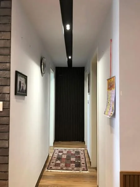 Hallway features: white painted walls, wooden flooring, recessed LED downlights, decorative wall clock, framed artwork, area rug with geometric pattern, dark wood accent wall, doorway leading to other rooms; style: modern.