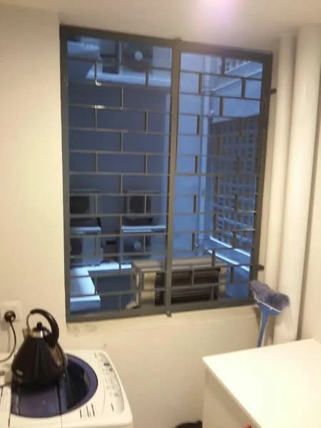 Laundry features: washing machine, white cabinetry, grey tiled walls, white walls, window with security bars, shelf above washing machine, kettle, broom, plumbing pipes visible.