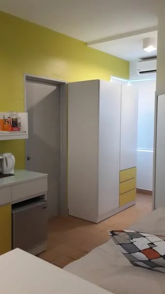 Room features: yellow painted walls, white cabinetry with yellow accents, built-in wardrobe, small refrigerator, kettle, light-colored flooring, air conditioning unit, door to another room; style: modern.