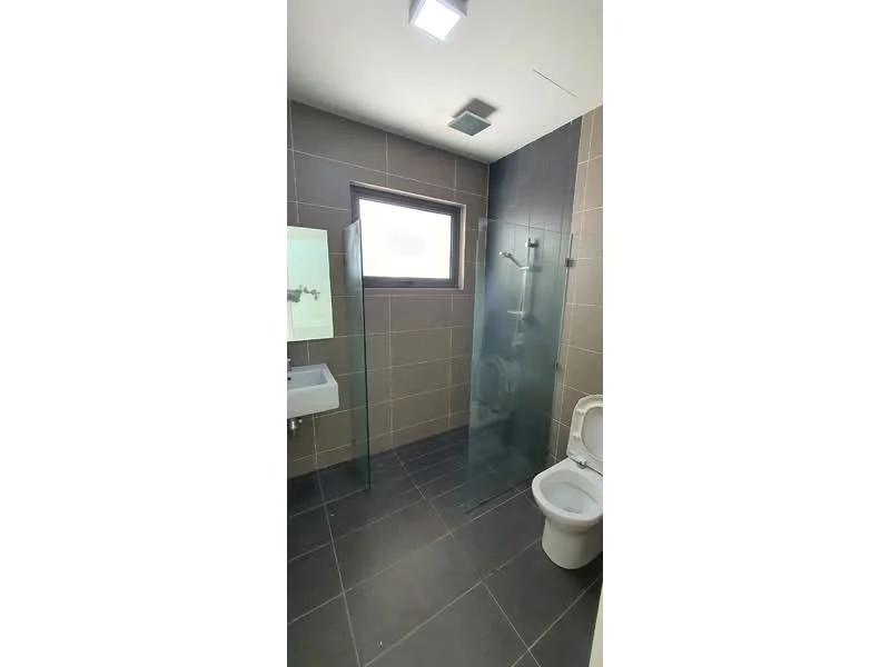 Bathroom features: grey tiled walls, dark grey floor tiles, walk-in shower with glass enclosure, chrome handheld shower, toilet, single-sink vanity with mirror, recessed ceiling lights, window for natural light; style: modern.