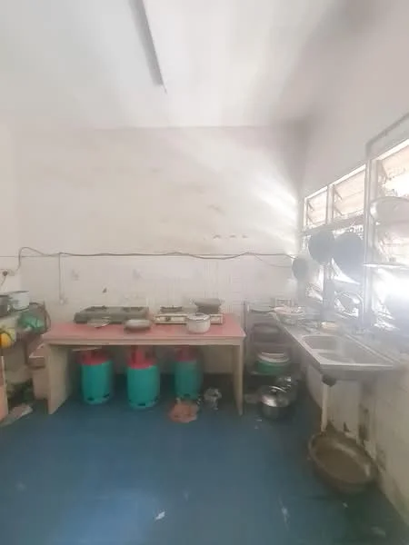 Kitchen features: blue vinyl flooring, white tiled walls, wooden countertop, stainless-steel sink, multiple cooking pots, gas cylinders, metal cooking utensils, open shelving, wall-mounted hooks for utensils.