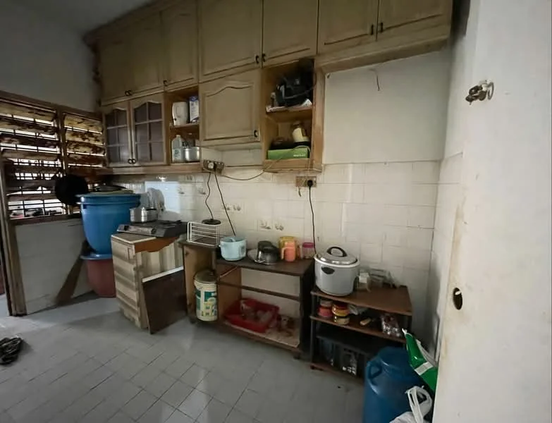 Kitchen features: wooden cabinetry with glass doors, white tiled walls, grey tiled flooring, countertop with appliances, rice cooker, plastic storage containers, sink, water dispenser, open shelving, wooden storage unit, multiple pots and pans, laundry basket.
