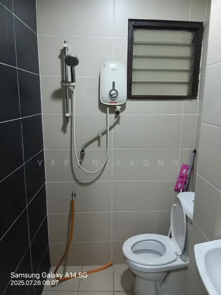 Bathroom features: white ceramic toilet, shower head with adjustable height, wall-mounted water heater, grey tiled walls, cream tiled flooring, window with horizontal slats, orange water pipe, toilet paper holder.
